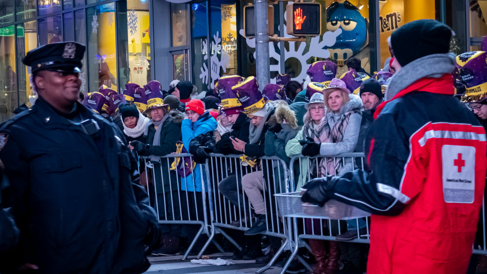 Police officer and Red Cross volunteer wearing a Red Cross vest stand outside in front of a crowd of people in Times Square, NYC.