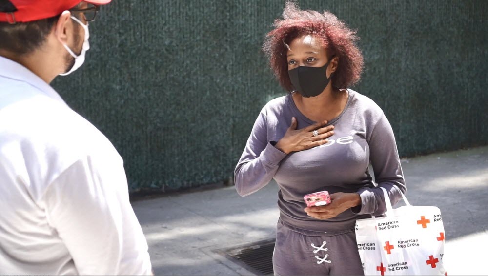 Red Cross volunteer wearing a face mask speaking to a woman outside.