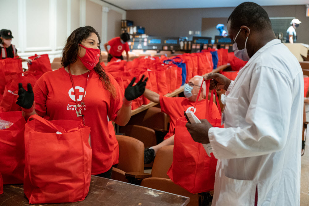 Red Cross workers dressed in red in a room filled with red bags.