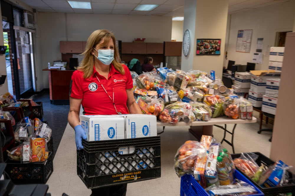 Red Cross female volunteer wearing a Red Cross tshirt carries food to be delivered. 