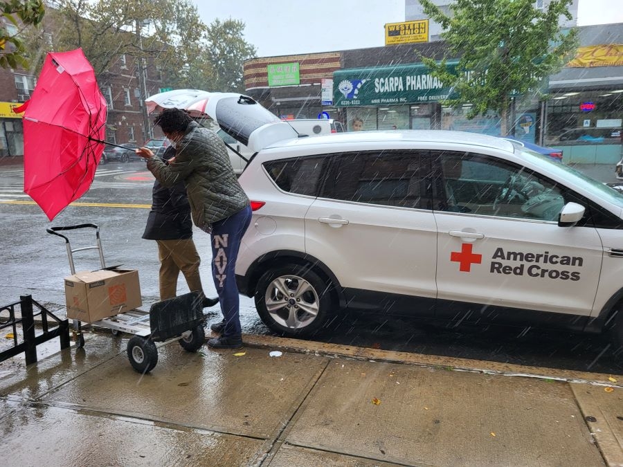 Martha Richardson battles her umbrella amidst a torrential downpour as Red Cross Hero Care Network caseworker Lallita Maharaj helps unload belongings from Martha's destroyed house.