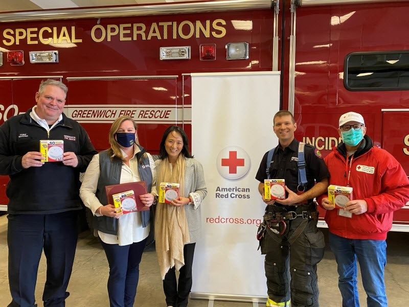 five people standing in front of a fire truck next to an American Red Cross Banner