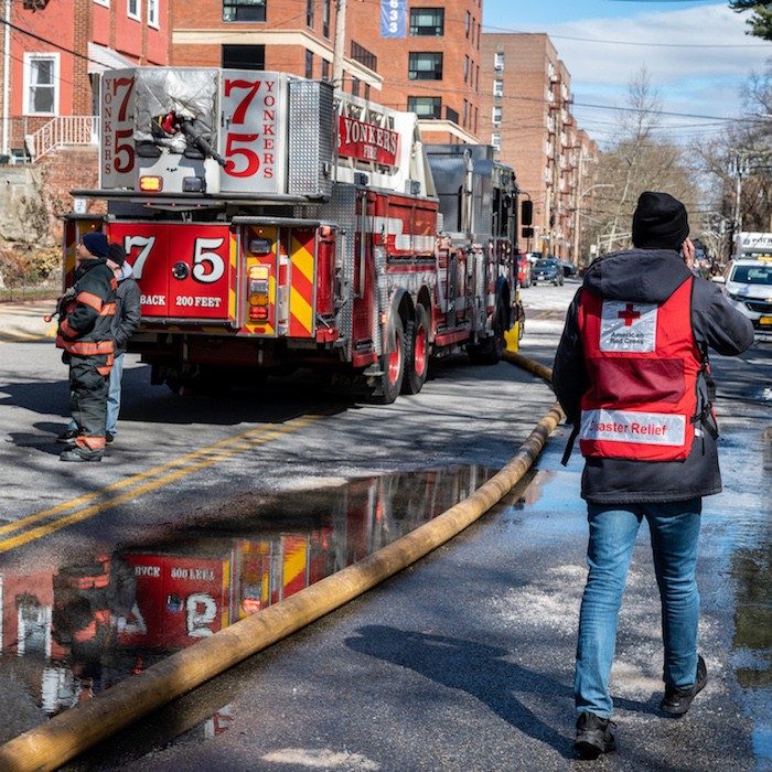 Red Cross disaster volunteer in a red vest next to a fire truck