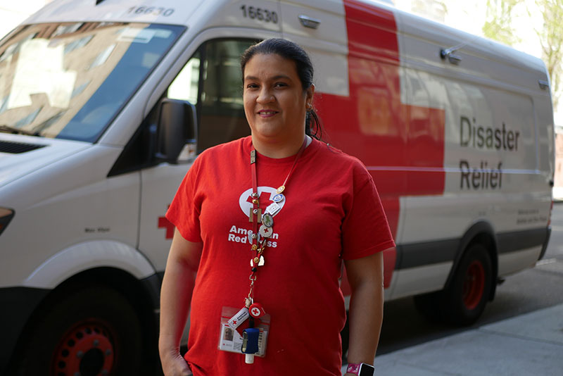 Jesennia Rodriguez wearing a Red Cross shirt and standing next to a Red Cross disaster relief van.