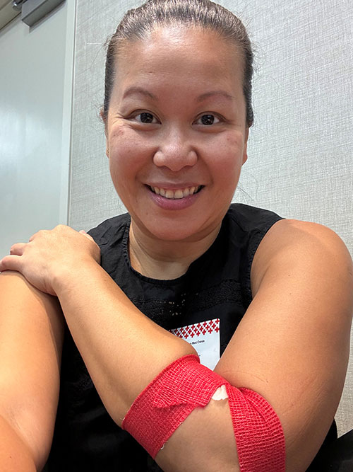 Lea Chiu-Adisa smiling while showing her red bandage around her arm after donating blood.