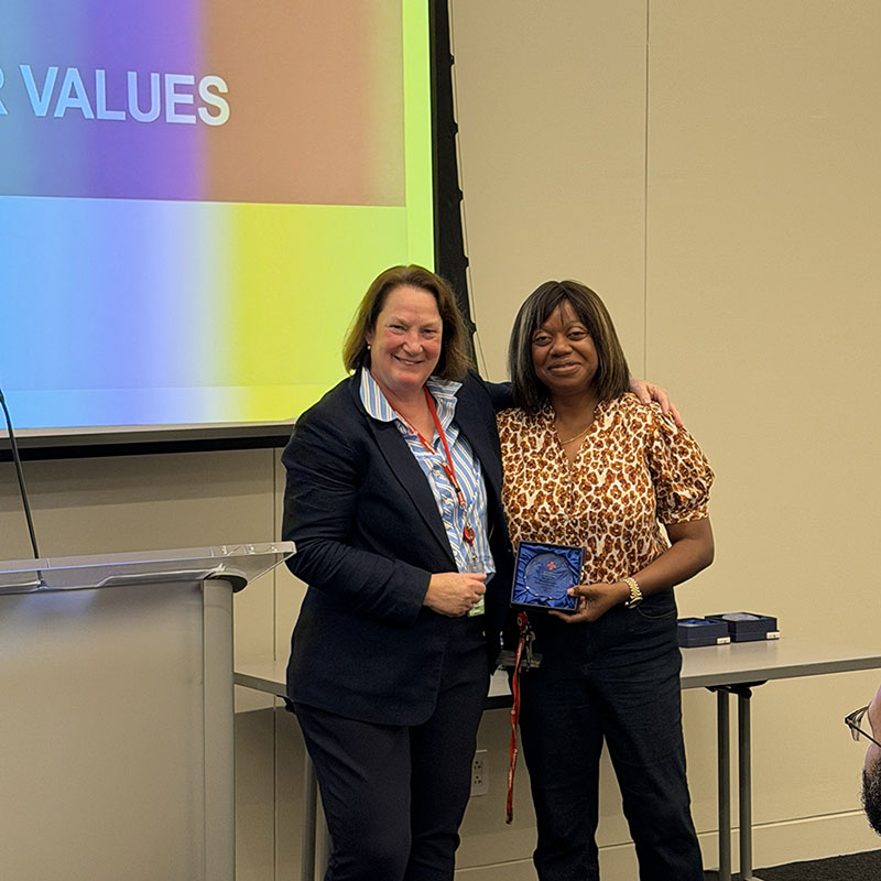 Norma Maynard holding a 5c award next to a Red Cross staff member at a Red Cross event.