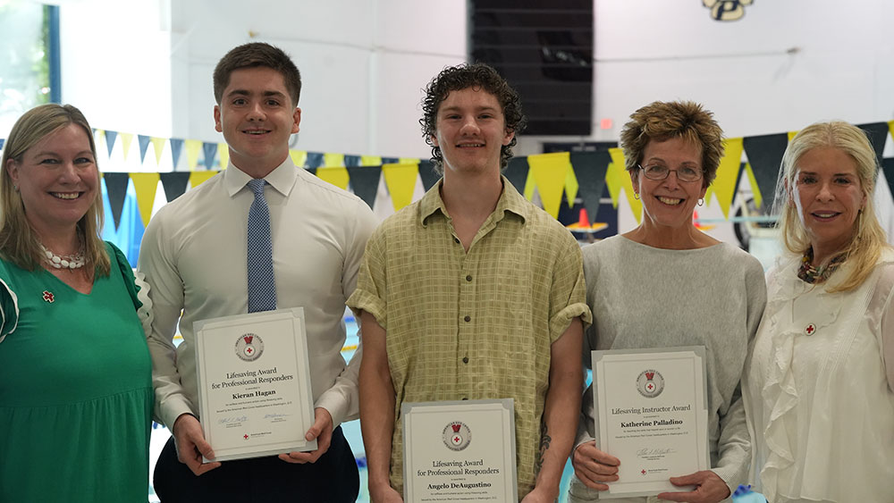 Two lifeguards and an instructor hold their Red Cross awards while standing next to two Red Cross employees.