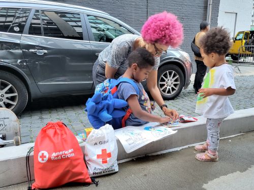 : A building resident colors with her two children, ages 23 months and 5 years, using a coloring book from a Red Cross kid kit.