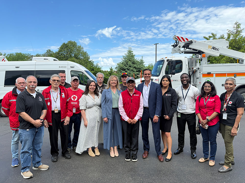 A diverse group of 15 people, including officials and volunteers, pose in front of utility vehicles under a clear blue sky.