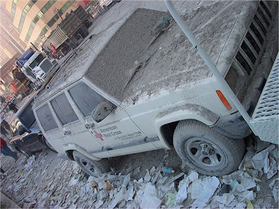 A Red Cross vehicle covered in ash and debris on the street next to ground zero.