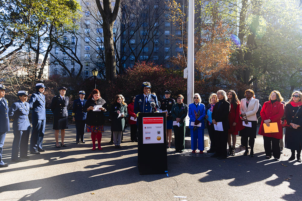Group of service women at event outside with one speaking at a podium.