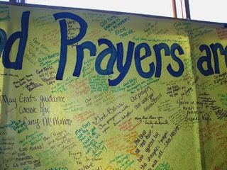 Close up of a yellow banner with the word "PRAYERS" and handwritten messages of support.
