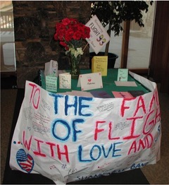 A table filled with cards and flowers. The front of the table is wrapped in a banner that says,  "to the families of flight 93, with love"