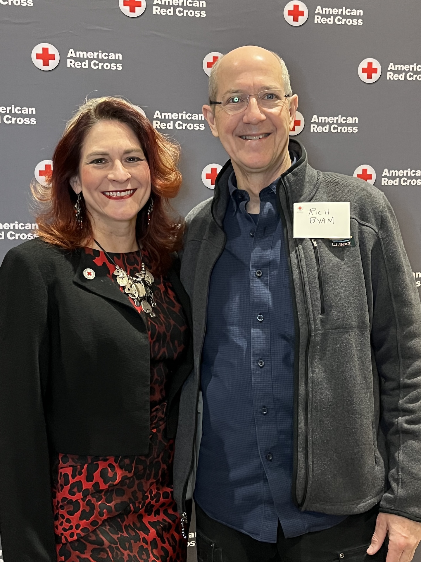 Kat Walsh and Rich Byam smiling in front of gray American Red Cross backdrop.