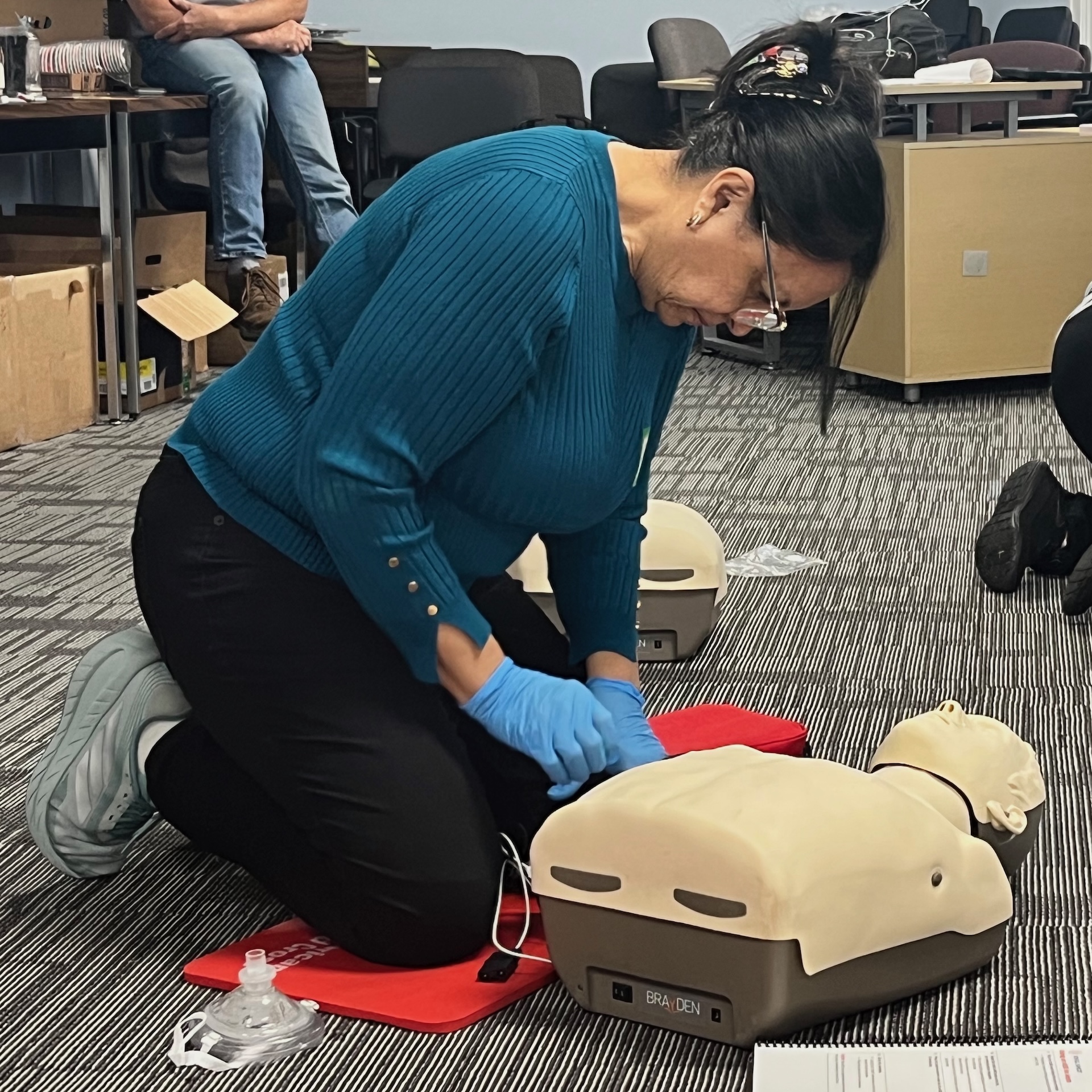 Carmen Carrasquel kneels next to a CPR manikin.