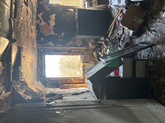 Bedroom damaged by fire, with black charred walls and ash covering the floor.