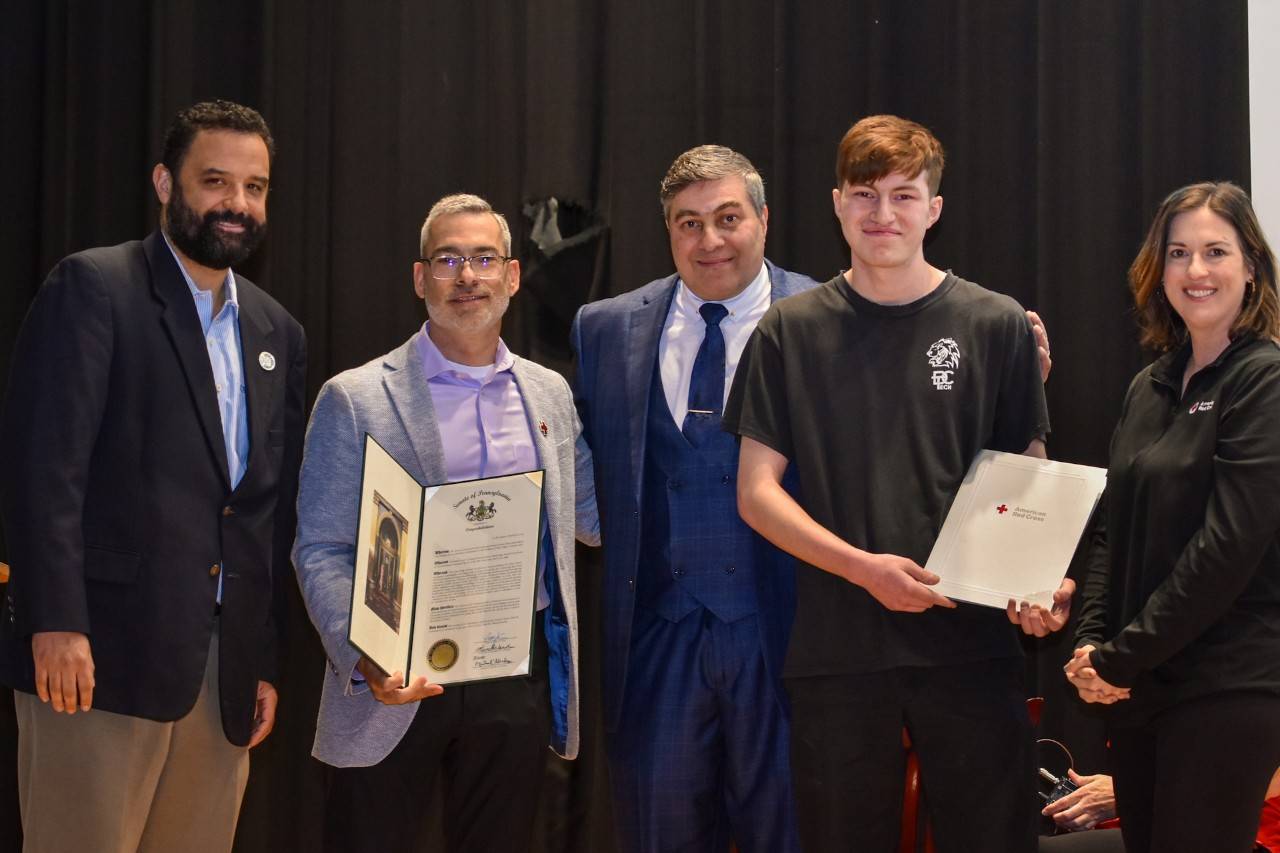 Five people pose for a photo, with two people holding award certificates
