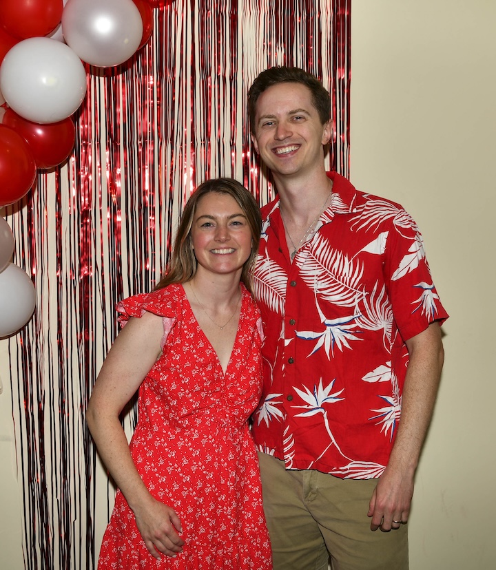 Kylie McCullough and her husband Peter smile in front of a red fringe background and balloons