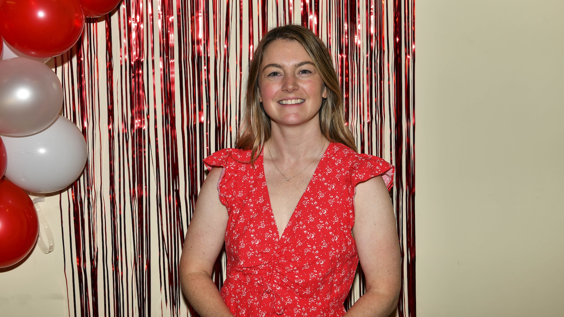 Kylie McCullough smiles in front of a red fringe backdrop and balloons