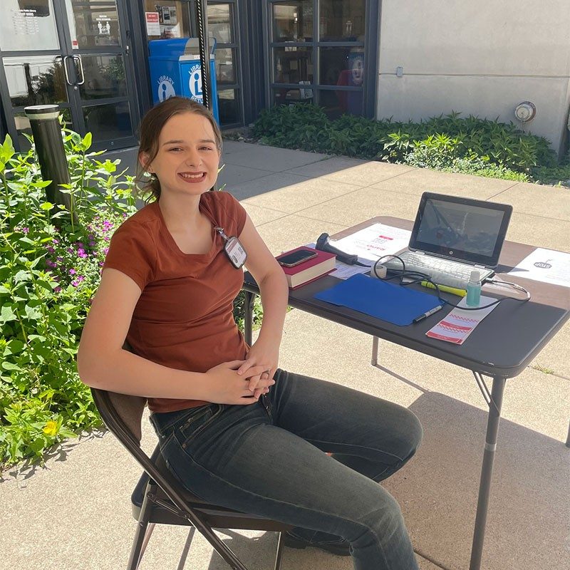 Rhiannon Costanzo sitting in chair at table in front of building