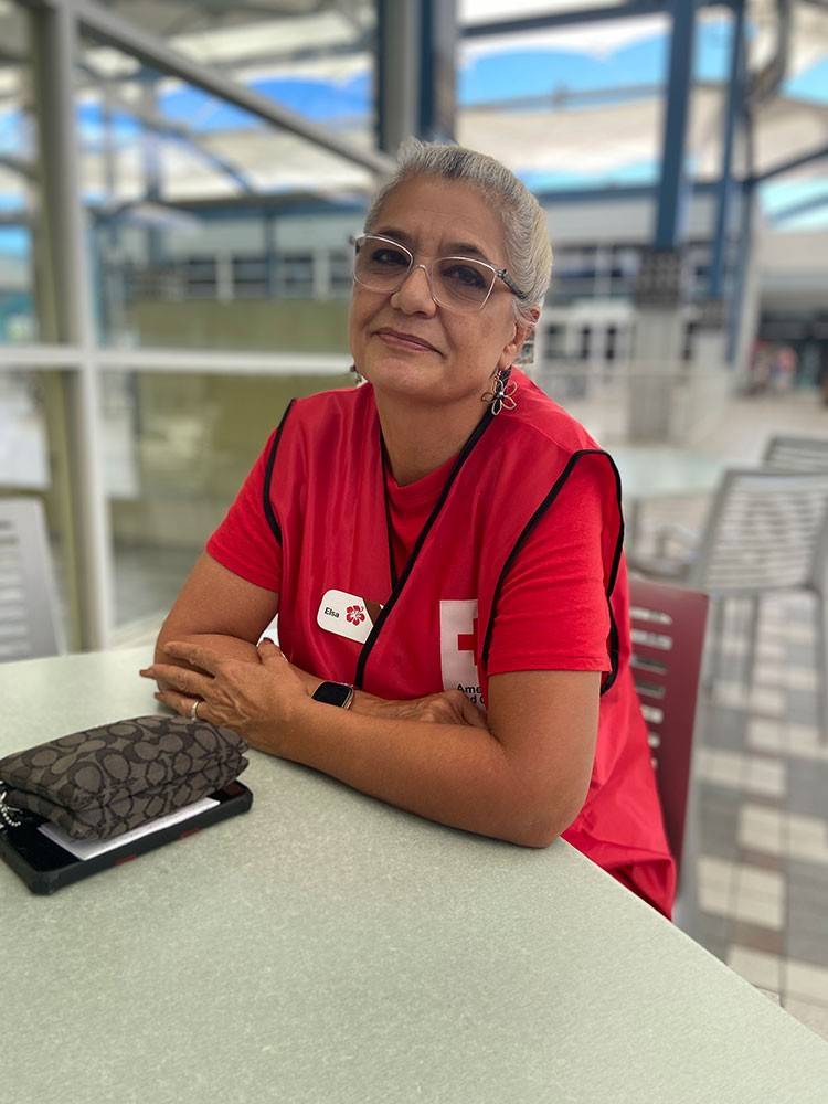 Red Cross volunteer sitting at a table wearing a Red Cross vest and glasses.