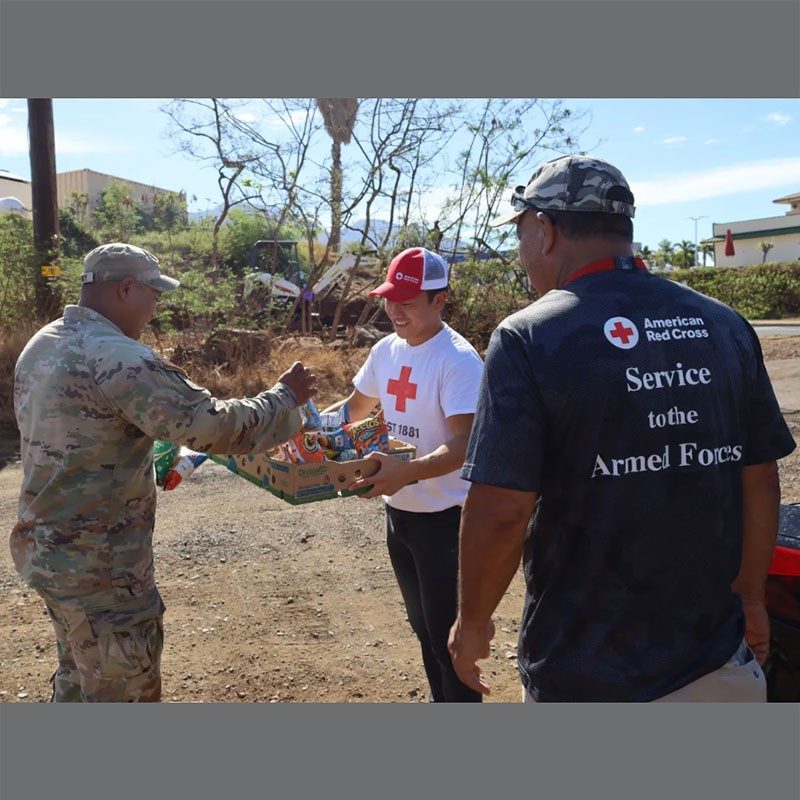 Red Cross volunteers handing out provisions to military member.