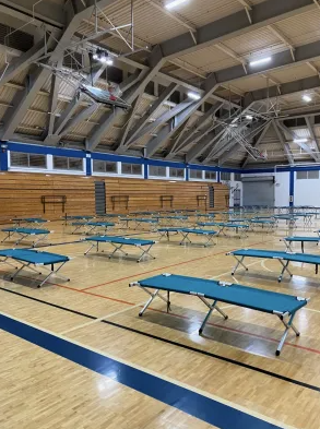 Cots lined up inside a gymnasium