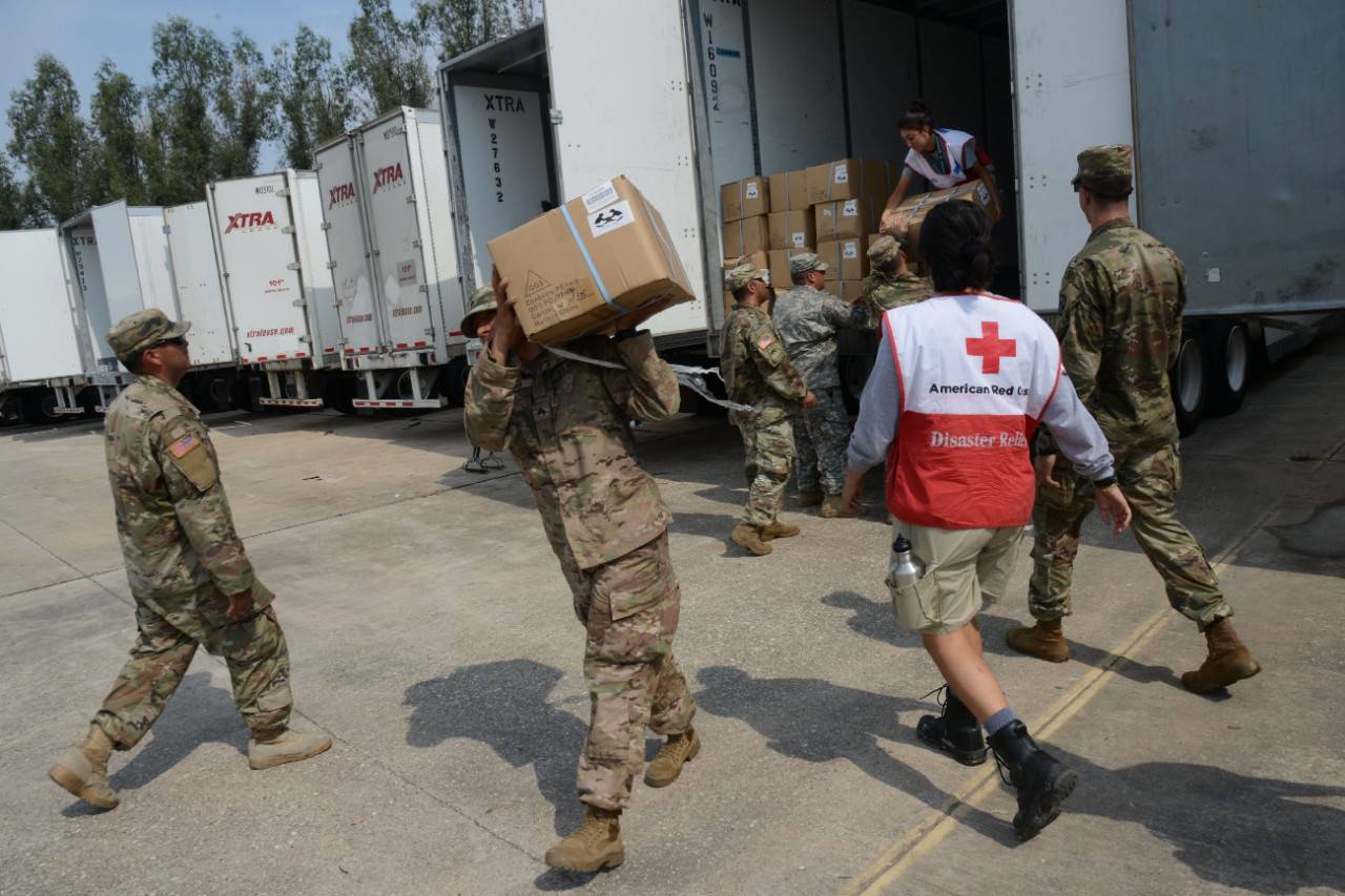 September 3, 2017. Red Cross Distribution Warehouse. Houston, Texas. Volunteers for the American Red Cross, members of AmeriCorps and active-duty US Army service members work together to load three convoys of Army high-profile vehicles with supplies. Two convoys are comprised of five trucks, the third is comprised of six trucks. Each truck is loaded with:
-	1 Payload of water or 2,184 bottles of water
-	1 payload of MREs
-	1 payload of clean-up kits or 48 clean- up kits
-	60 shovels
-	60 rakes
-	1 pallet of trash bags or 144 boxes of trash bags
-	1 pallet of tarps
Total combined materials being moved by the three convoys equals:
-	16 payloads of water or 34,944 bottles of water
-	16 payloads of MREs
-	16 payloads of clean-up kits or 768 clean-up kits
-	960 shovels
-	960 rakes
-	16 pallets of trash bags or 2,304 boxes of trash bags
-	16 pallets of tarps
All of these supplies and trucks were loaded in just three hours of partnership work. Photo by Daniel Cima for the American Red Cross
