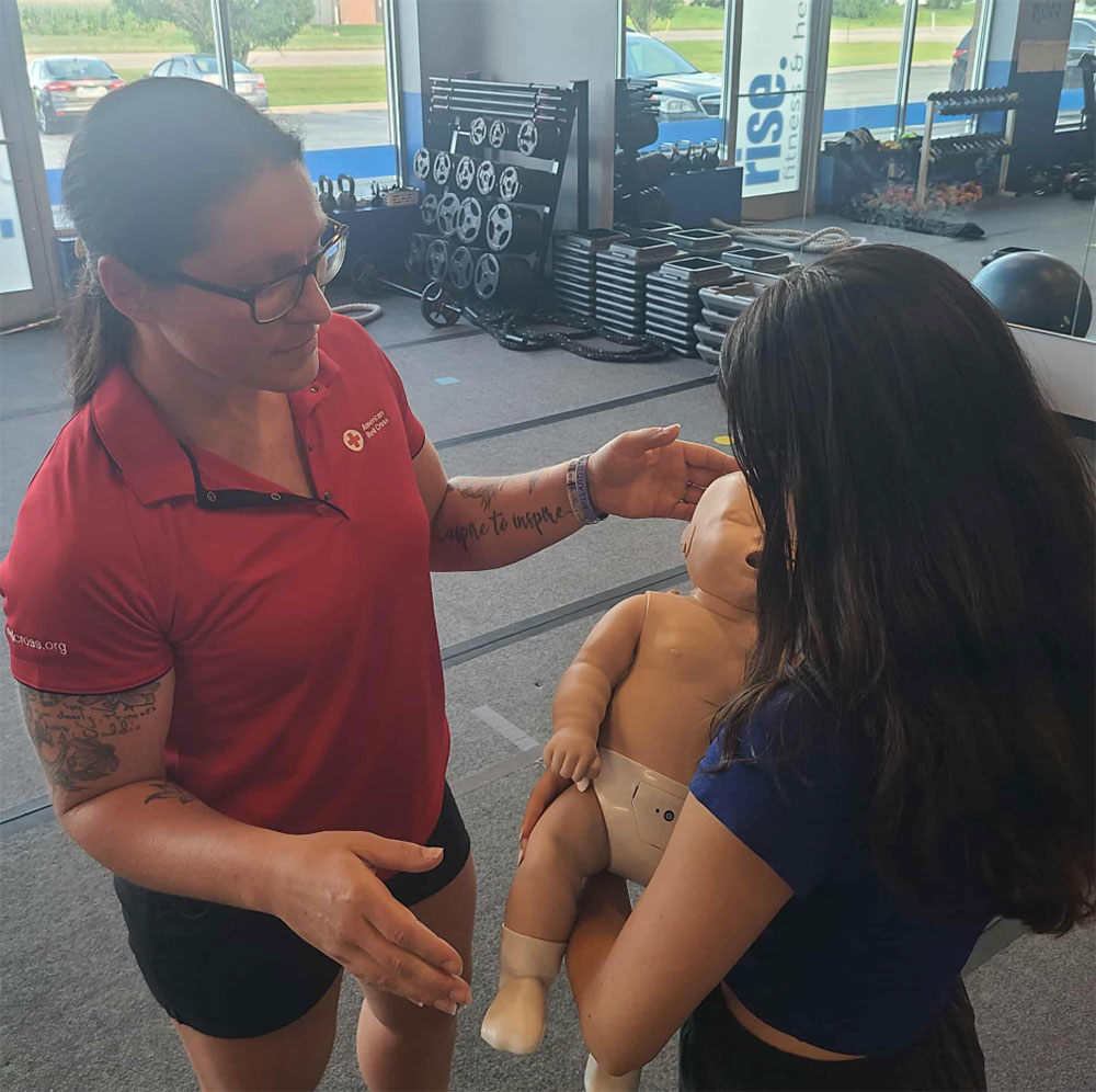 Amber Marchetta standing next to a girl who is holding a CPR manikin baby.