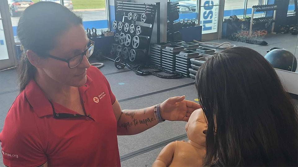 Amber Marchetta standing next to a girl who is holding a CPR manikin baby.