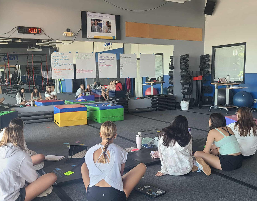 young women sitting on the floor in a CPR training classroom.