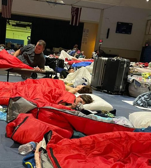 the inside of a Red Cross shelter with people on cots in sleeping bags.