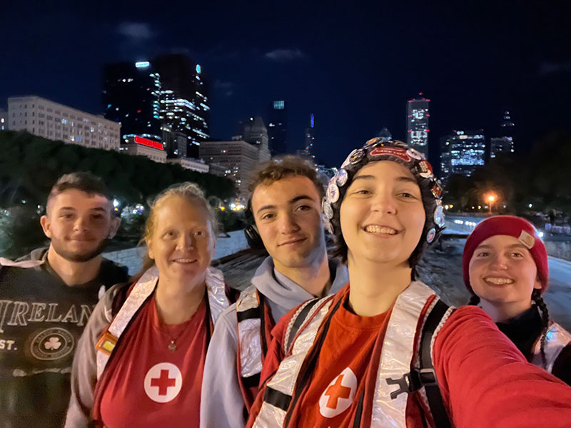 group picture of the Speciale Family at night wearing Red Cross vests and with the city buildings and lights in the background.