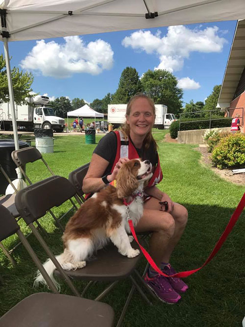 Red Cross volunteer Jackie Speciale petting a small dog that's sitting on a chair under a canopy.