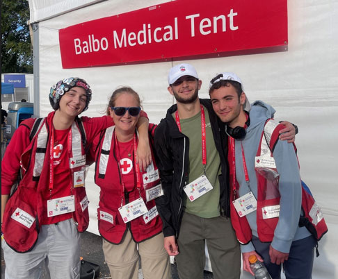 group picture of the Speciale Family wearing Red Cross vests and standing next to the Balbo Medical Tent.