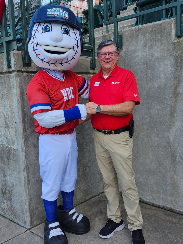 Terry Brewster giving a fist bump to a mascot with a baseball head.