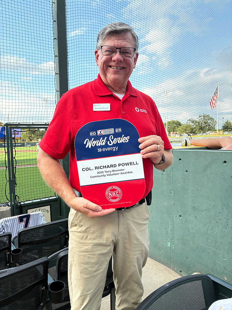 Terry Brewster holding the Terry Brewster award in the stands of a baseball field.