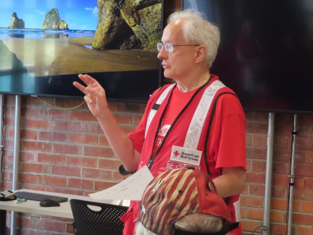 Red Cross volunteer wearing Red Cross vest and speaking at a podium.