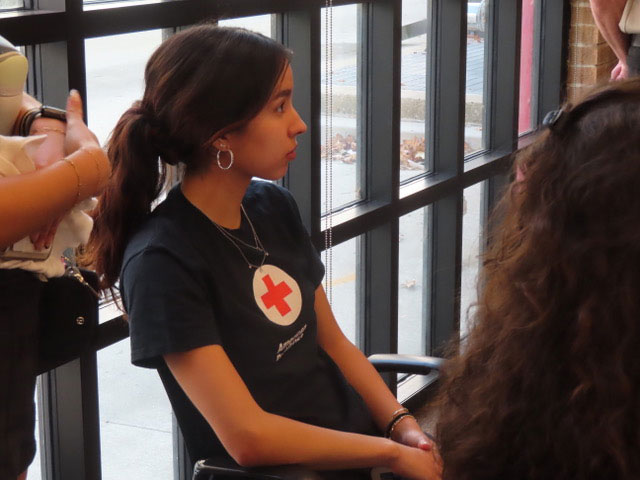 Daniela Beers sitting in chair, wearing a Red Cross shirt and listening to instructions.