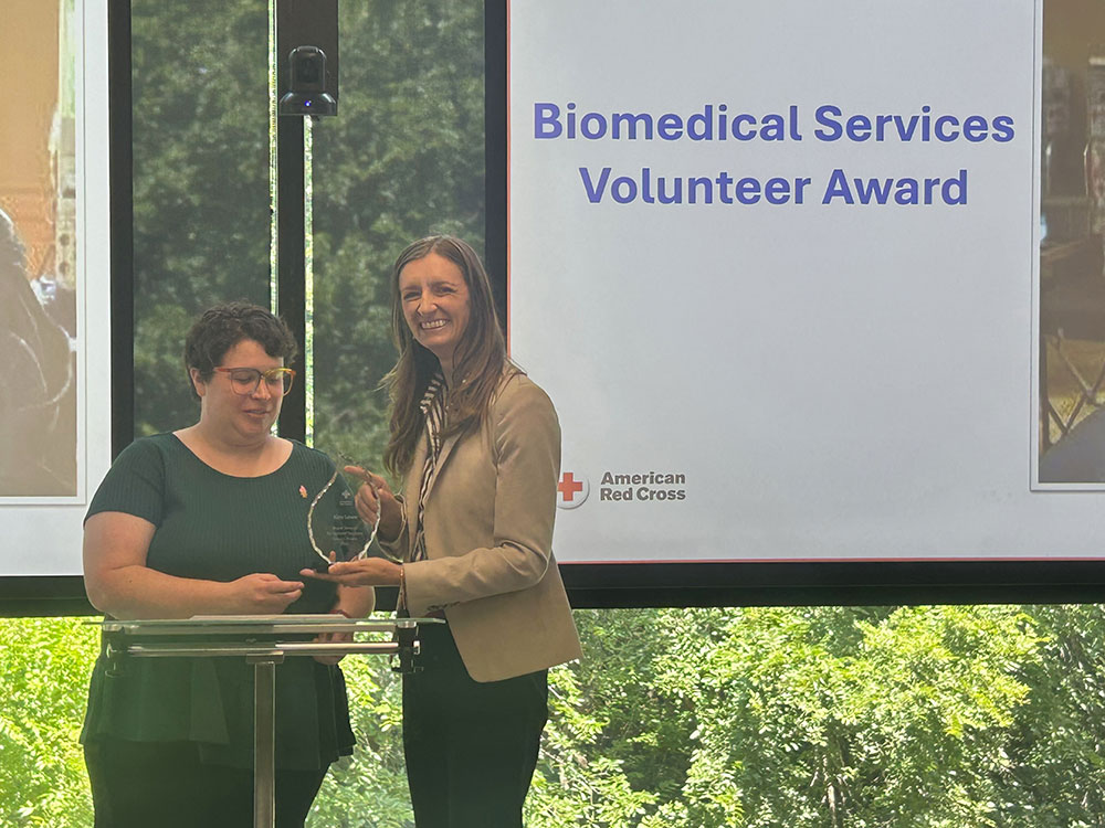 Kim Lowe being presented the 2025 volunteer award on stage at an event.