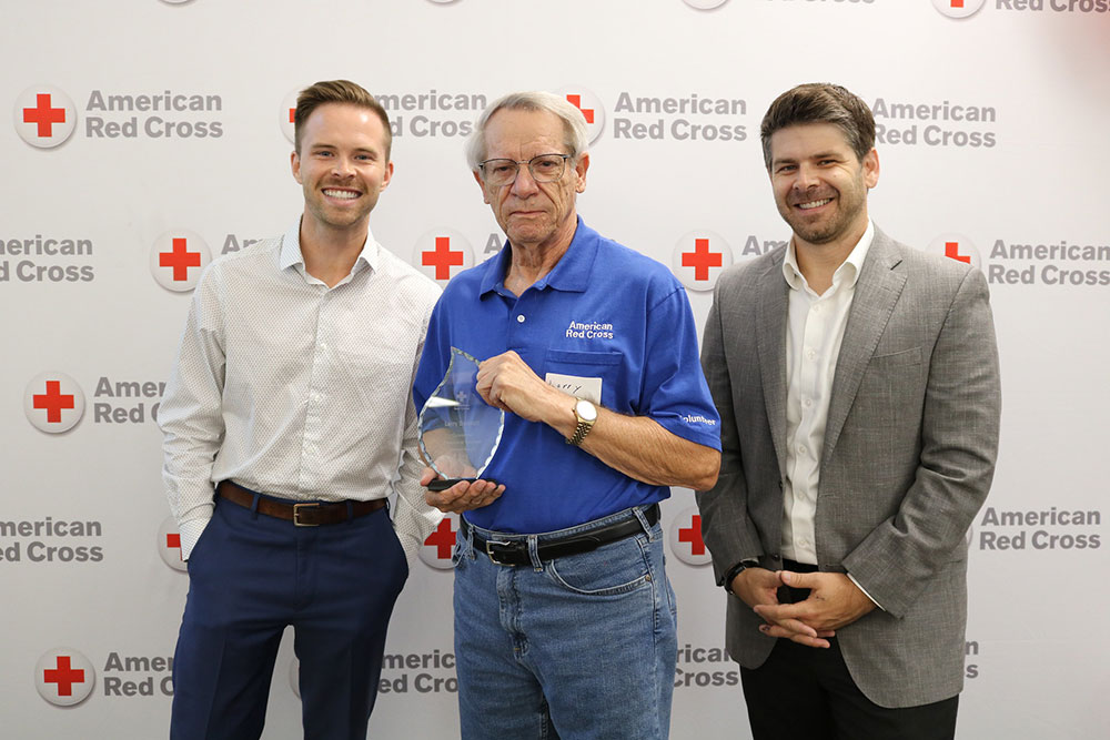 Larry Bennett holding a Red Cross award and standing next to two Red Cross staff members.