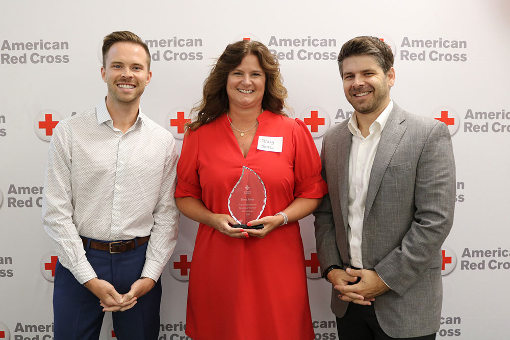 Stacy Jones holding a Red Cross award and standing next to two Red Cross staff members.