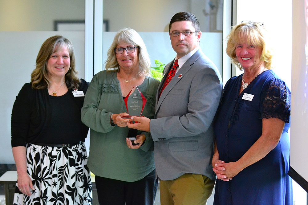 Toni Floyd, Community Disaster Program Managers Carol Arnold and Kyle Lewis, and Executive Director Jane Blocher stand together, proudly holding an award, smiling at the camera. 