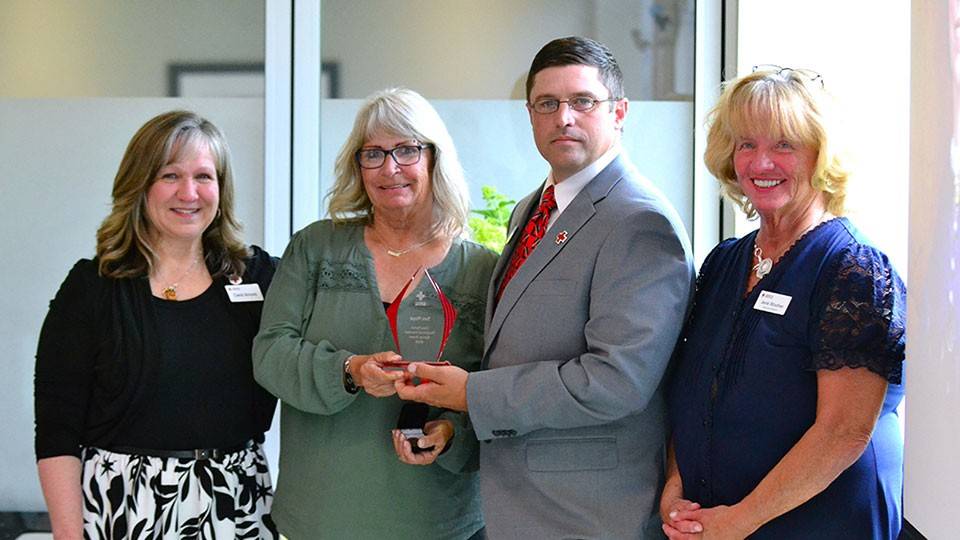 Toni Floyd, Community Disaster Program Managers Carol Arnold and Kyle Lewis, and Executive Director Jane Blocher stand together, proudly holding an award, smiling at the camera. 