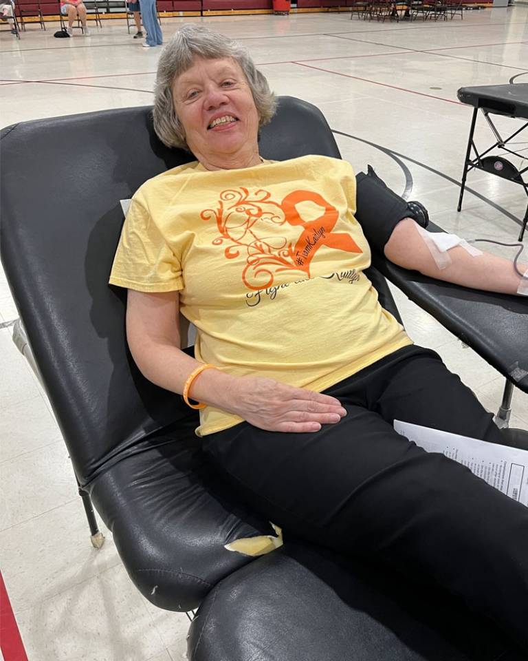 A person in a yellow shirt that reads "Fight like Kaitlyn" donates blood on a donation bed at a Red Cross blood drive.