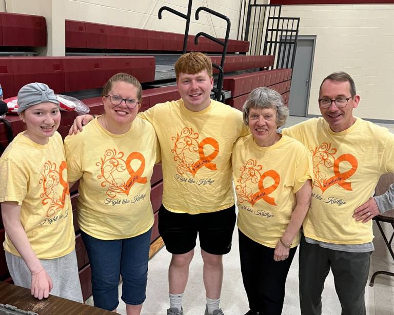 A family of five wearing yellow shirts that read "Fight like Kaitlyn" smile at the camera at a blood drive.