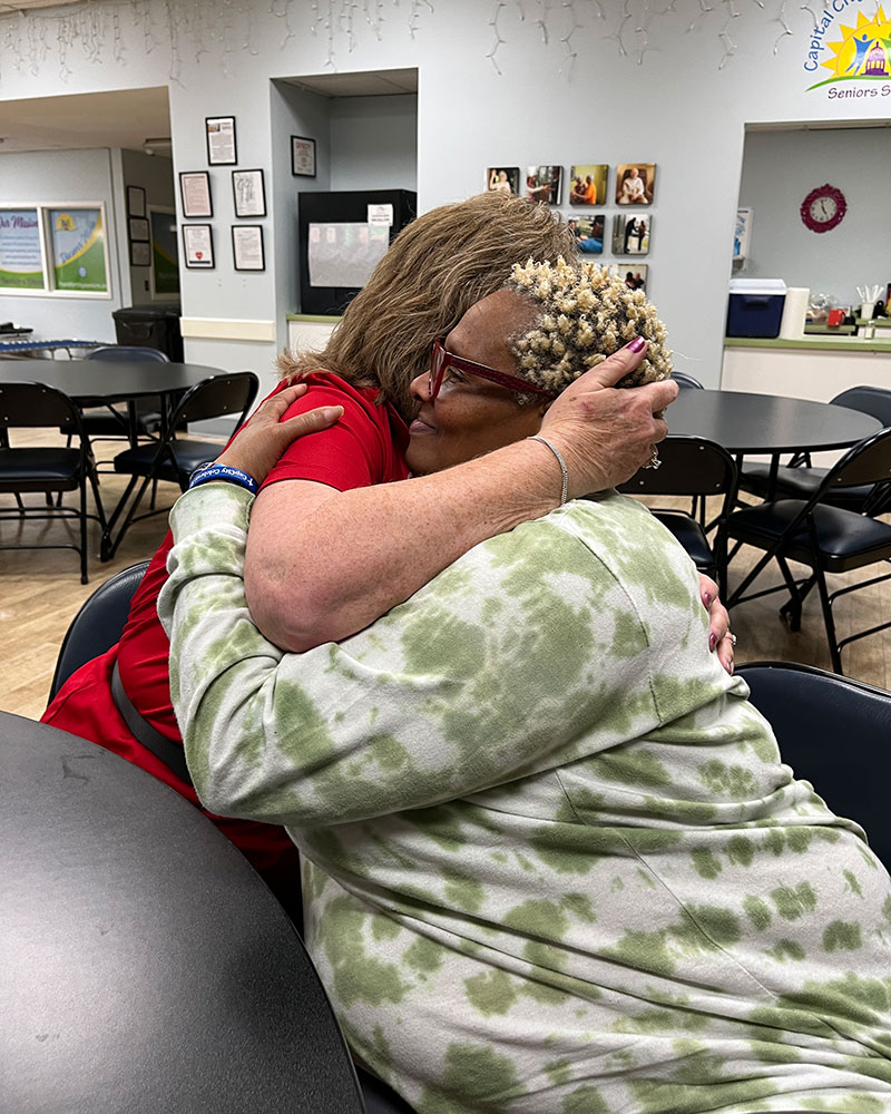 red cross volunteer Donna McCollum hugs Debra Love at a table.