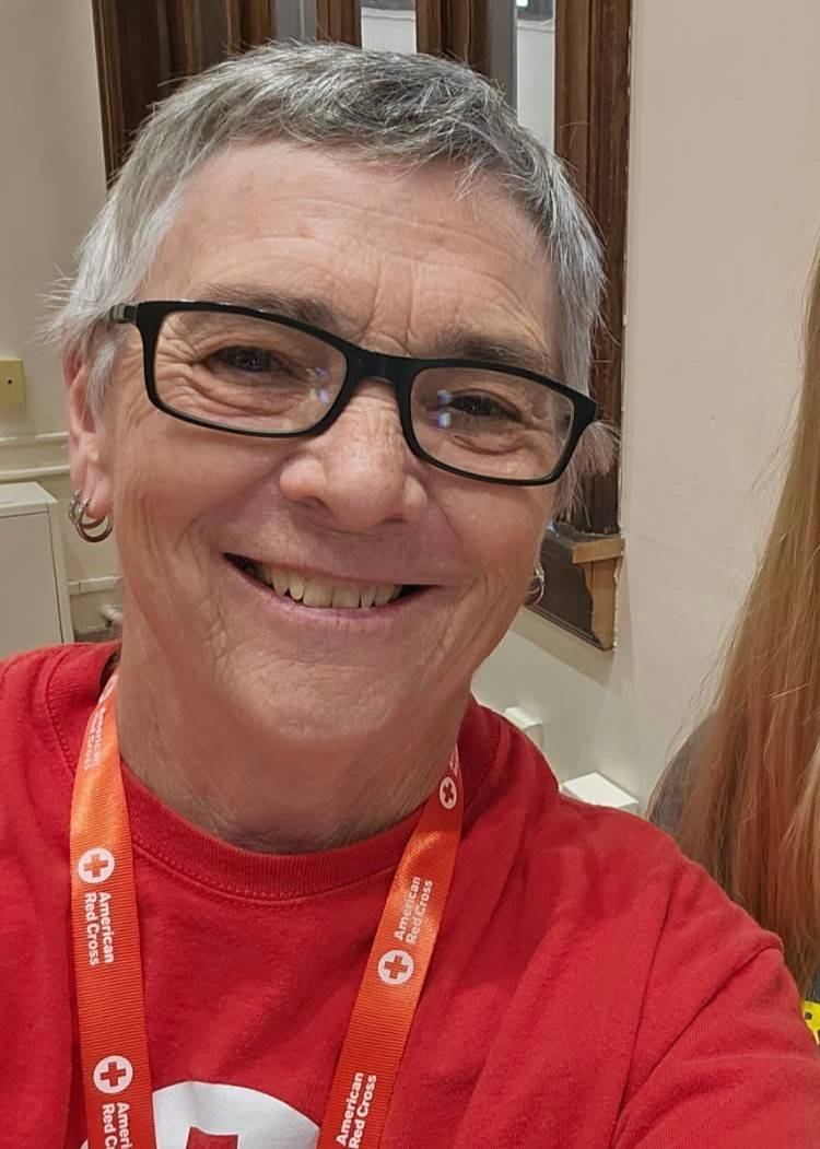 A Red Cross volunteer in a red t-shirt and lanyard smiles at the camera.