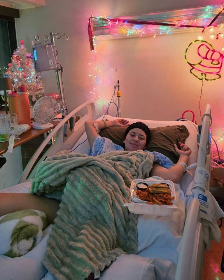 A young woman lays in a hospital bed under a teal blanket.
