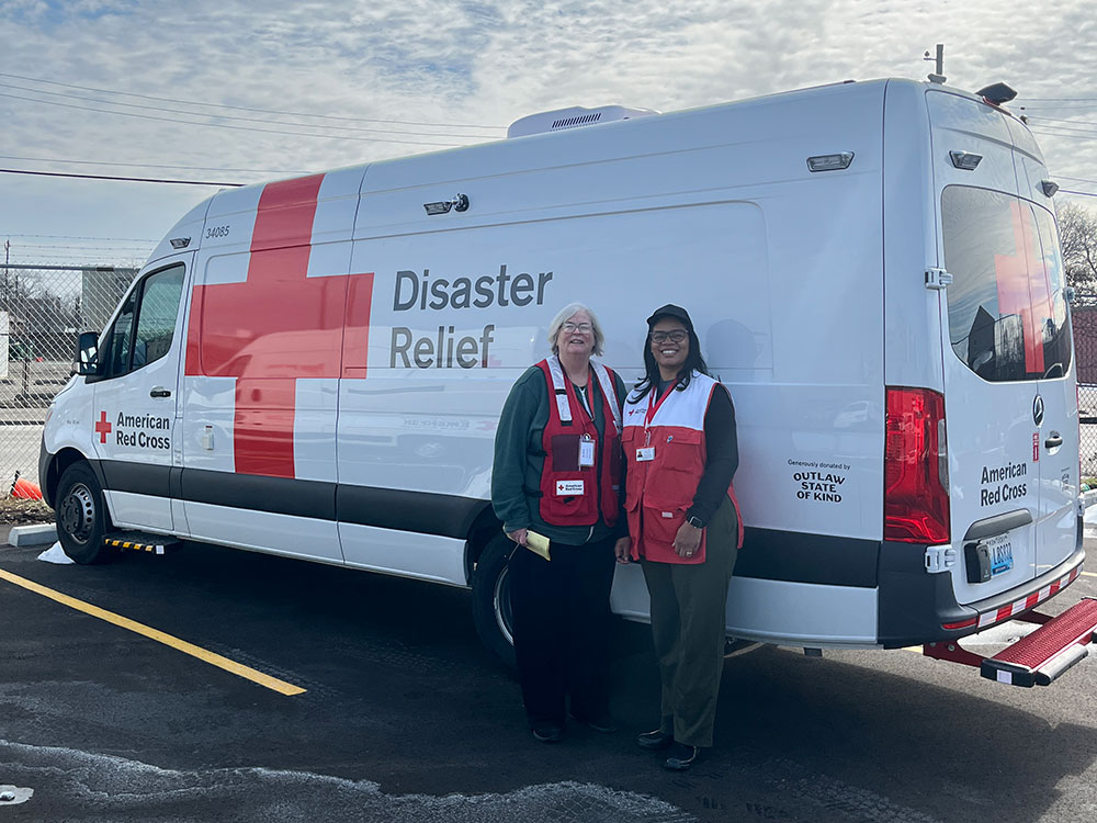 Two Red Cross volunteers standing next to Red Cross disaster relief vehicle in a parking lot.